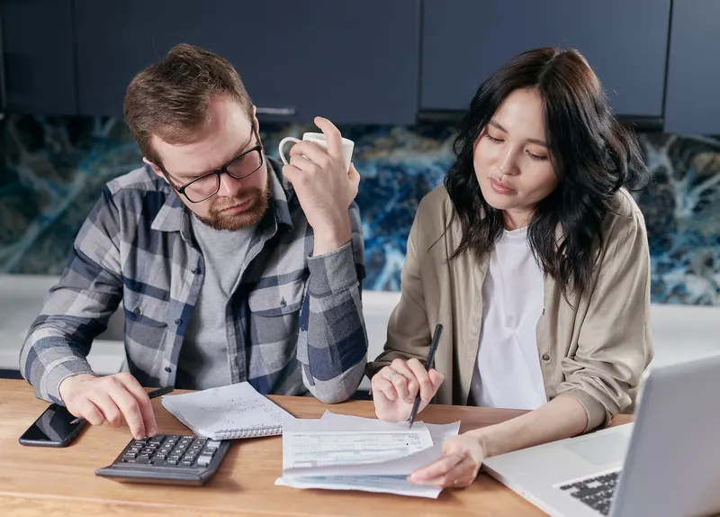 Cuplu calculând bugetul, cu facturi și calculator pe masă