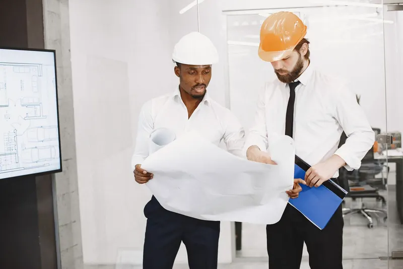 Doi specialiști cu căști de protecție verificând planurile construcției